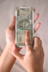A person holding a stack of 500 Indian Rupee banknotes in one hand, with the other hand pointing at the notes. The person is wearing a ring with a decorative design.