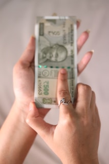 A person holding a stack of 500 Indian Rupee banknotes in one hand, with the other hand pointing at the notes. The person is wearing a ring with a decorative design.