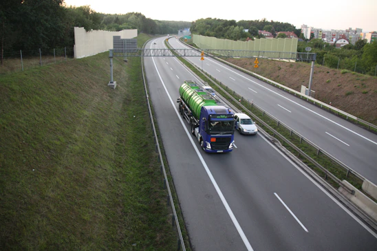 A sturdy truck carrying freight on a highway with pipelines running alongside under a clear sky.