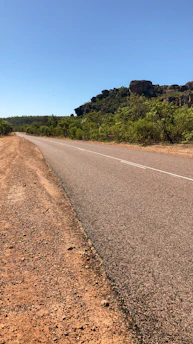 A freshly paved highway stretching through a lush Cameroonian landscape under a clear blue sky.
