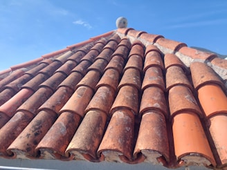Close-up of a roofer carefully laying tiles on a sloped roof under a clear sky.