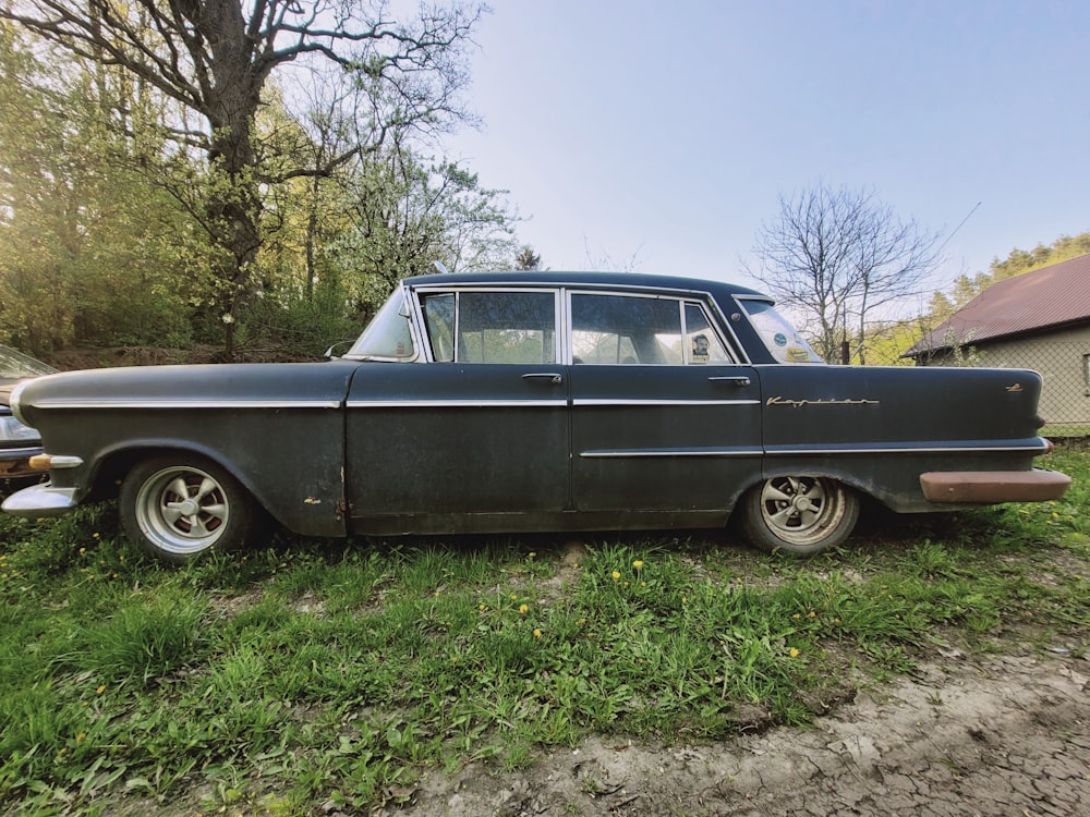 an old black car is parked in the grass