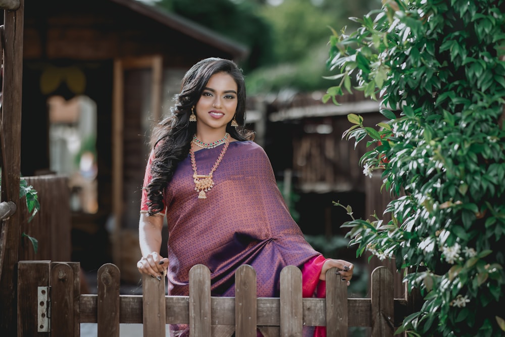a woman in a purple sari standing on a wooden fence