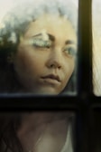 An artistic shot of a woman looking thoughtfully out of a window with soft natural light.