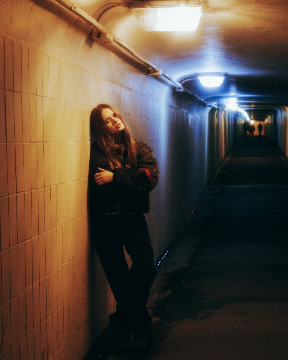 a woman leaning against a wall in a tunnel