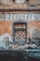 A weathered, old building facade with a blocked-up window made of bricks and surrounded by peeling, faded paint in earthy tones. The word 'HOSTINEC' is prominently displayed above the window in aged letters.