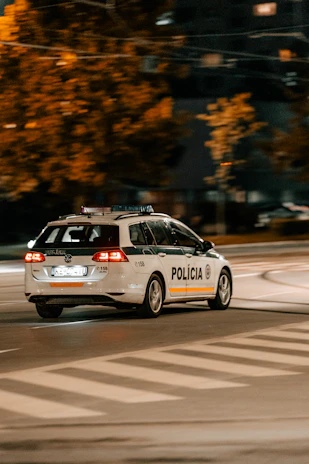 Police patrol car speeding through urban traffic with sirens on at night.