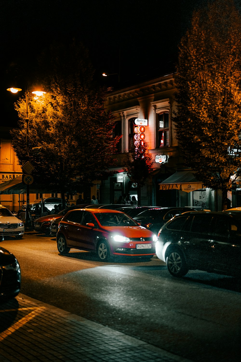 a city street at night with cars parked on the side of the road