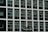Two construction workers in hard hats stand on a suspended platform, cleaning the windows of a tall building that features a grid-like pattern of glass panes and white frames.