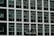 Two construction workers in hard hats stand on a suspended platform, cleaning the windows of a tall building that features a grid-like pattern of glass panes and white frames.
