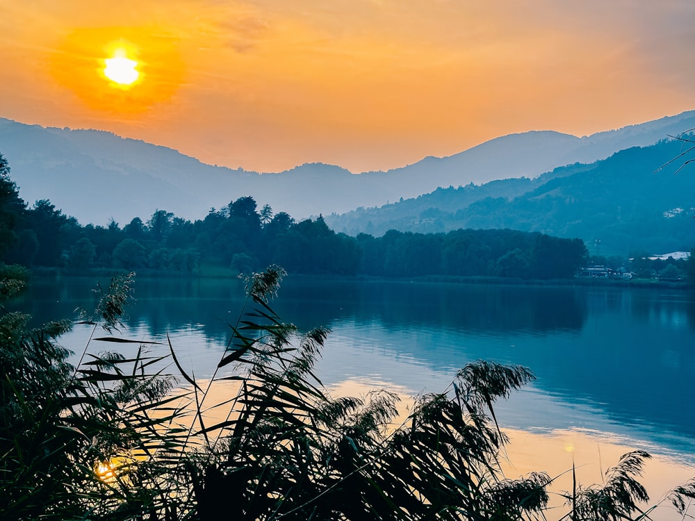 the sun is setting over a lake with mountains in the background