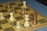 A close-up view of a chessboard featuring several chess pieces in the middle of a game. The pieces are made of wood, with a mix of light and dark tones. The board has a classic checkered pattern and is positioned on a blue surface.