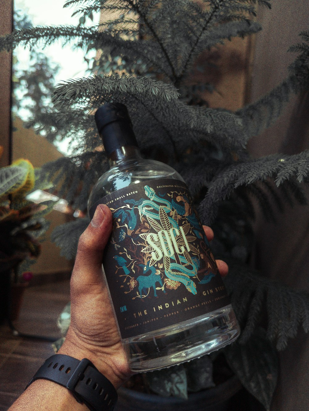 a person holding a bottle of alcohol in front of a christmas tree