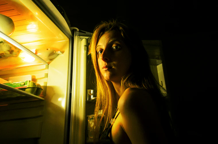 Mujer mirando dentro de la refrigeradora de noche