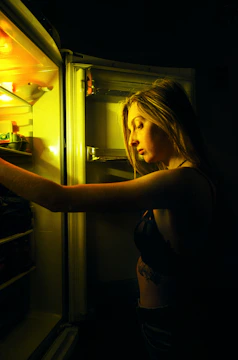 Close-up of a technician inspecting the inside of a refrigerator with a bright yellow toolbox nearby.