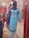 A mannequin is dressed in a light blue embroidered kurta with white floral patterns, paired with a matching blue dupatta. The mannequin is displayed in a clothing store with a red and white interior. Various fabrics and garments are visible in the background.