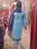 A mannequin is dressed in a light blue embroidered kurta with white floral patterns, paired with a matching blue dupatta. The mannequin is displayed in a clothing store with a red and white interior. Various fabrics and garments are visible in the background.