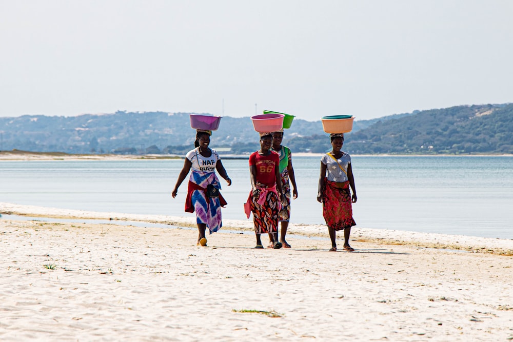 three people walking on a beach carrying buckets on their heads