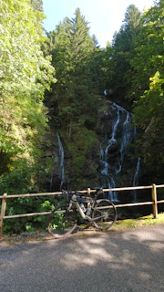Group of cyclists pausing beside a sparkling waterfall surrounded by dense vegetation