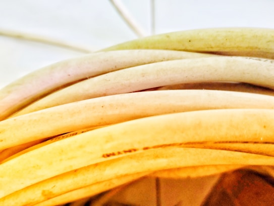 Several coiled, light-colored cables or wires with a smooth texture are stacked in close proximity, capturing a portion of their surface. The lighting highlights subtle gradients and shadows on the curved surfaces.