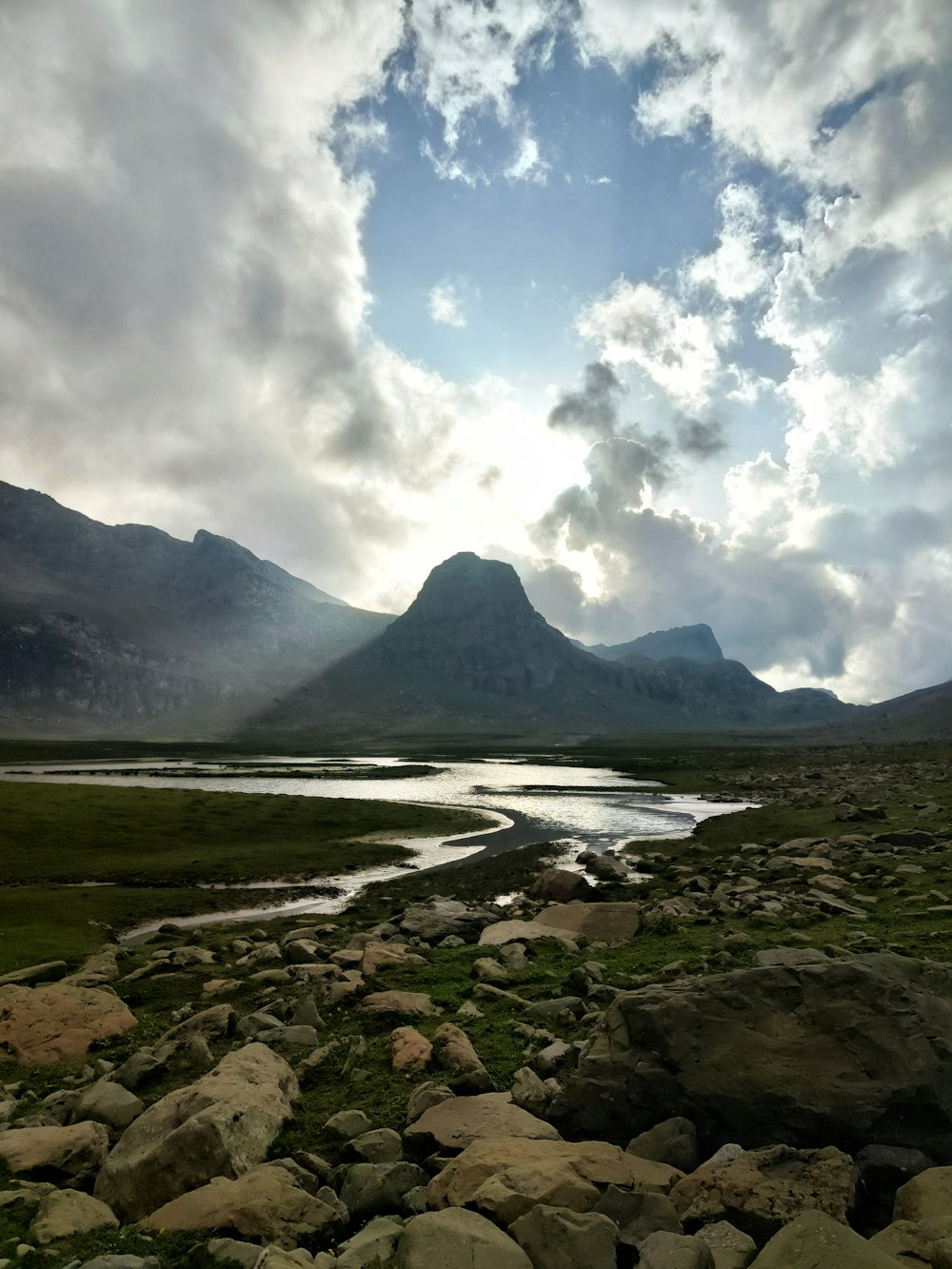 a river running through a lush green field under a cloudy sky