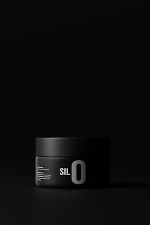 A black cylindrical container with minimalistic white text, labeled with 'SILO'. The container has a matte finish and is set against a dark background, creating a sleek and modern appearance.