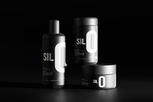 Three black cylindrical containers are displayed against a dark background. Each features bold white typography with the letters 'SIL O' prominently visible. The sleek, minimalist design emphasizes a modern aesthetic.