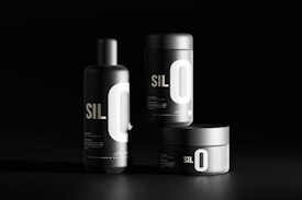 Three black cylindrical containers are displayed against a dark background. Each features bold white typography with the letters 'SIL O' prominently visible. The sleek, minimalist design emphasizes a modern aesthetic.