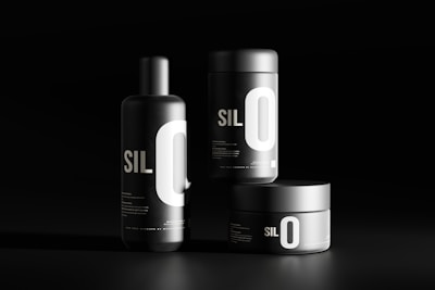 Three black cylindrical containers are displayed against a dark background. Each features bold white typography with the letters 'SIL O' prominently visible. The sleek, minimalist design emphasizes a modern aesthetic.