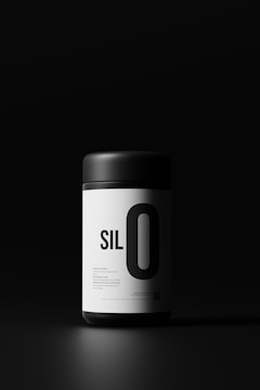 A sleek, cylindrical container with a matte black lid and a white label displaying bold black text. The lighting emphasizes the minimalistic and modern design against a dark background.