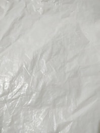 Crumpled and textured white surface with subtle shadows and highlights, resembling plastic or fabric material.