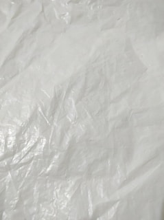 Crumpled and textured white surface with subtle shadows and highlights, resembling plastic or fabric material.