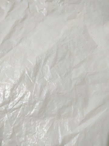 Crumpled and textured white surface with subtle shadows and highlights, resembling plastic or fabric material.