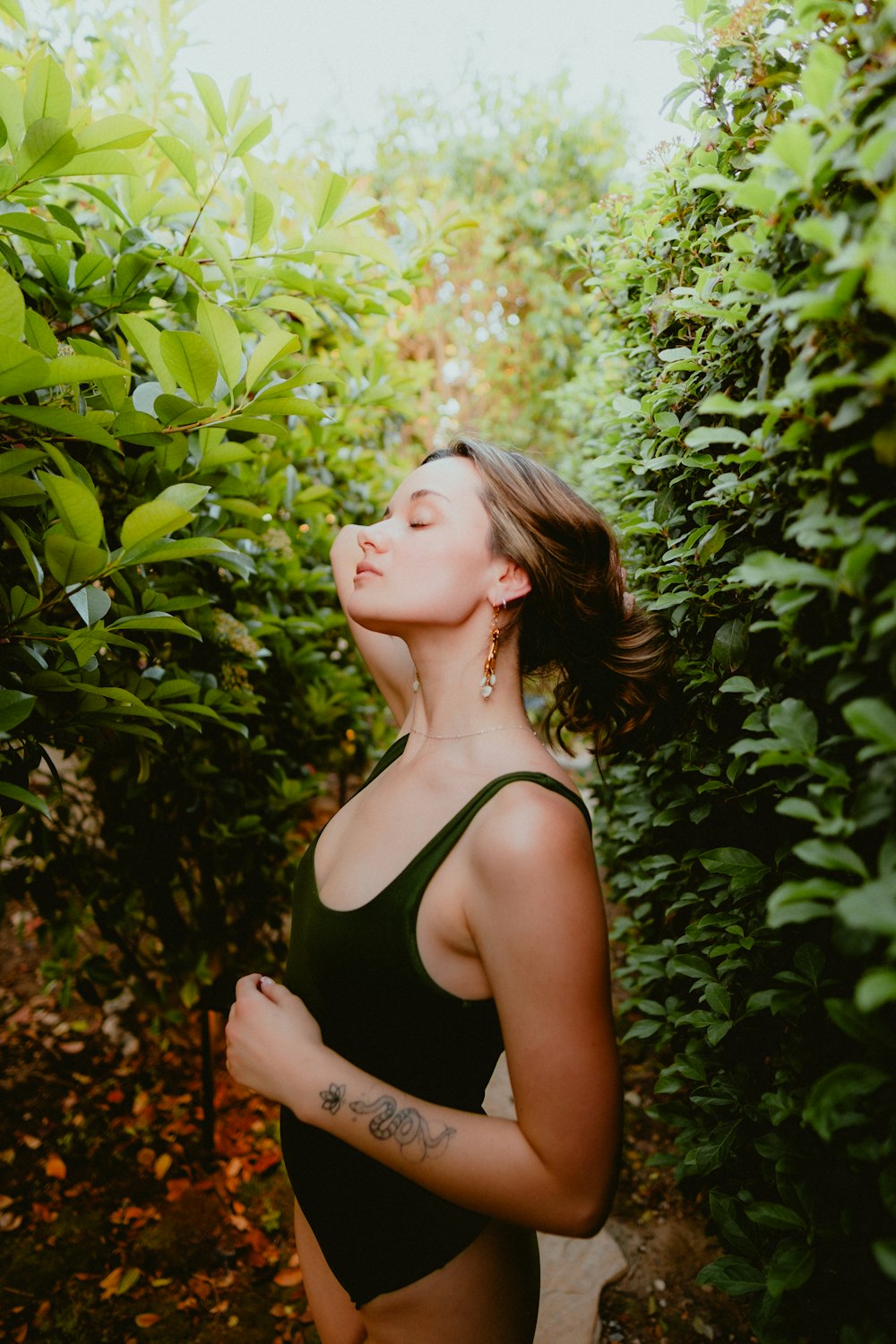 a woman in a black bathing suit standing in front of a bush