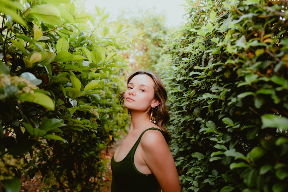 a woman standing in between two rows of bushes
