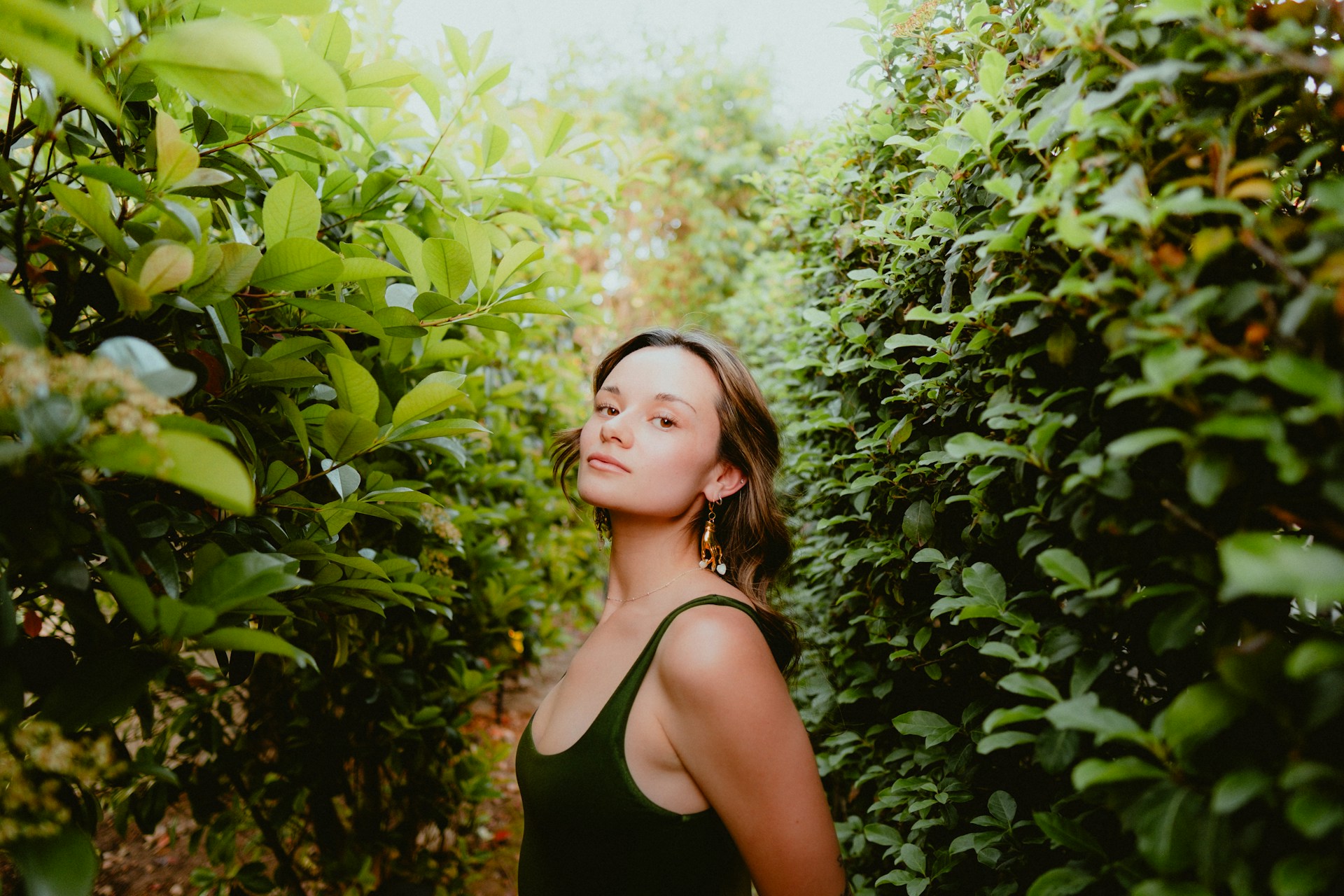 a woman standing in between two rows of bushes