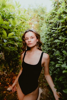 a woman in a black swimsuit walking through a bush