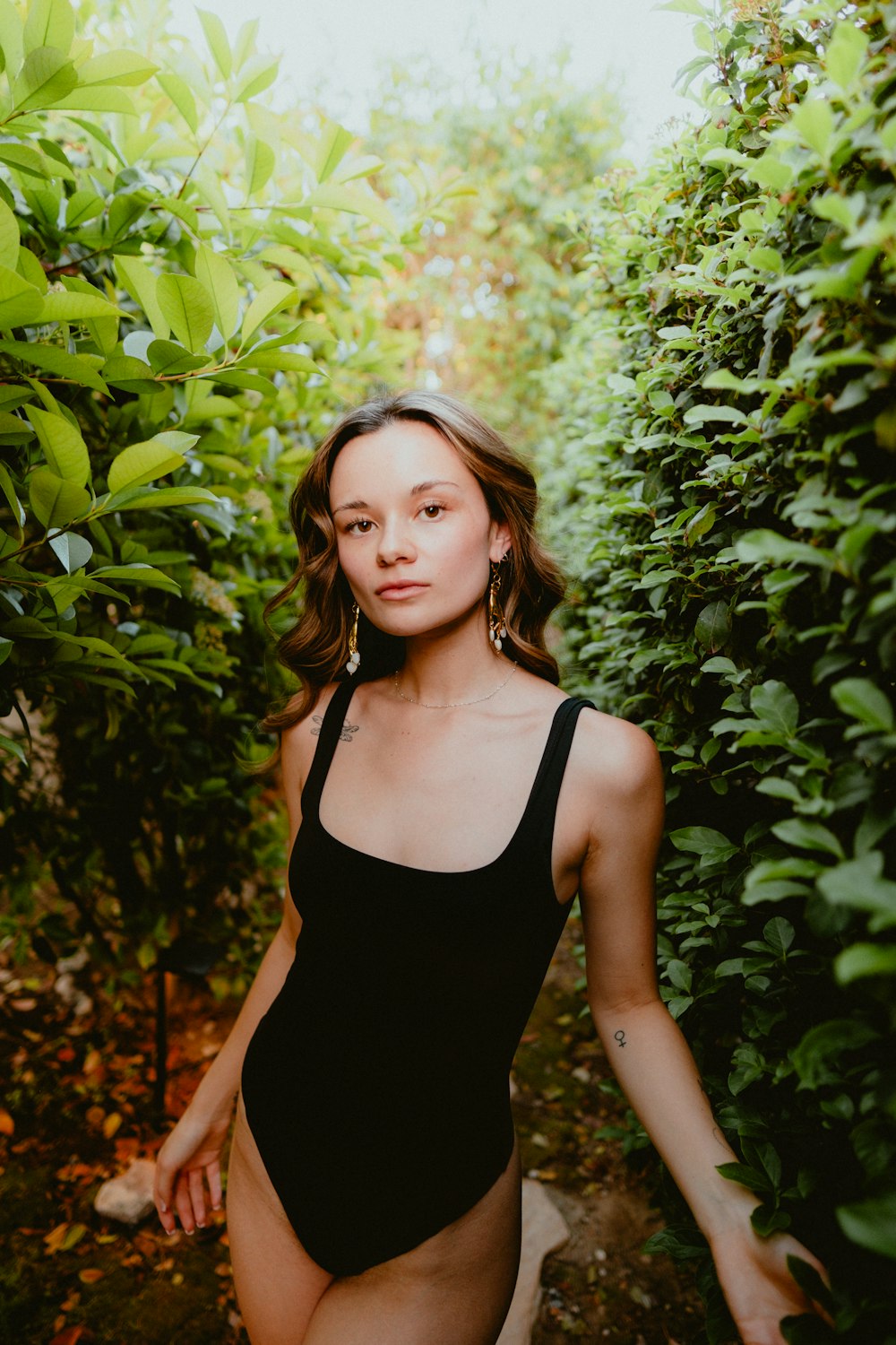 a woman in a black swimsuit walking through a bush