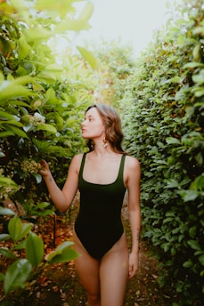a woman in a black swimsuit standing in a bush