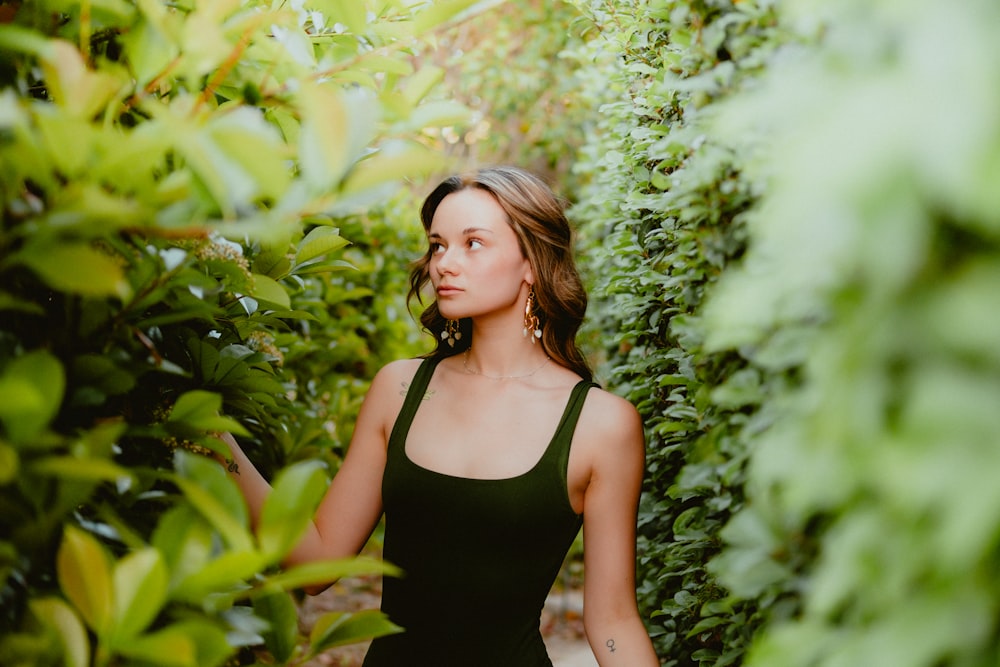 a woman in a black dress standing in front of a bush