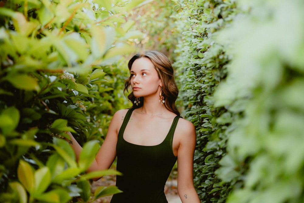 una mujer con un vestido negro de pie frente a un arbusto