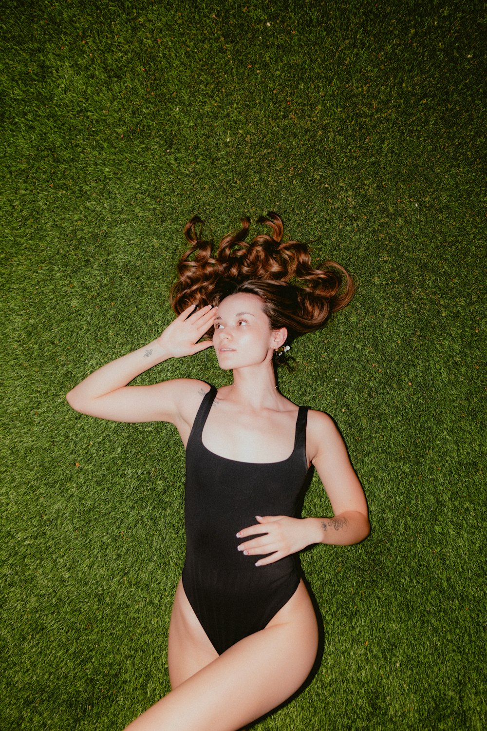 a woman in a black swimsuit laying on the grass