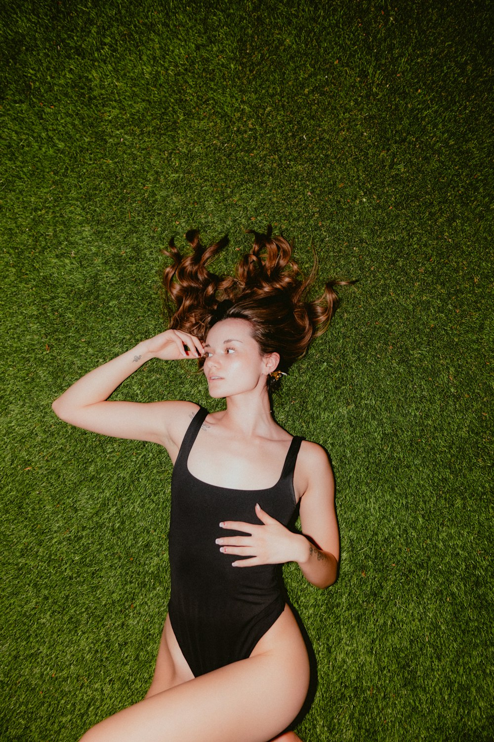 a woman in a black swimsuit laying on the grass