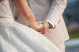 Close-up of a bride and groom holding hands with wedding rings visible.