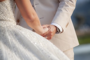 A close-up of a bride’s hand gently holding a groom’s, lit by soft, dramatic shadows.