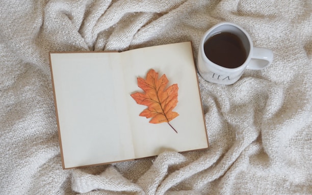 An open e-book on a tablet surrounded by a cup of tea and autumn leaves.