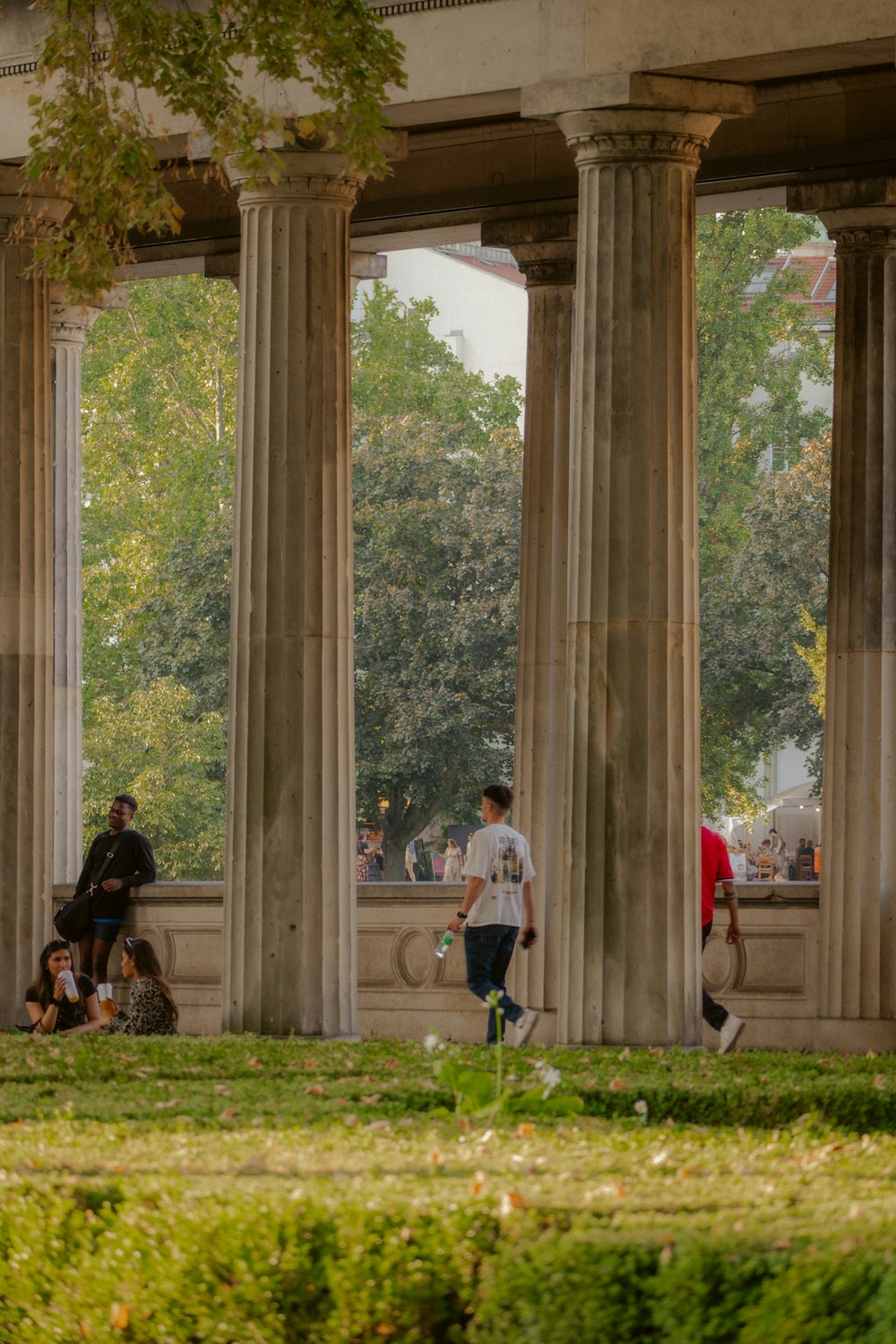 a group of people walking down a sidewalk next to tall pillars