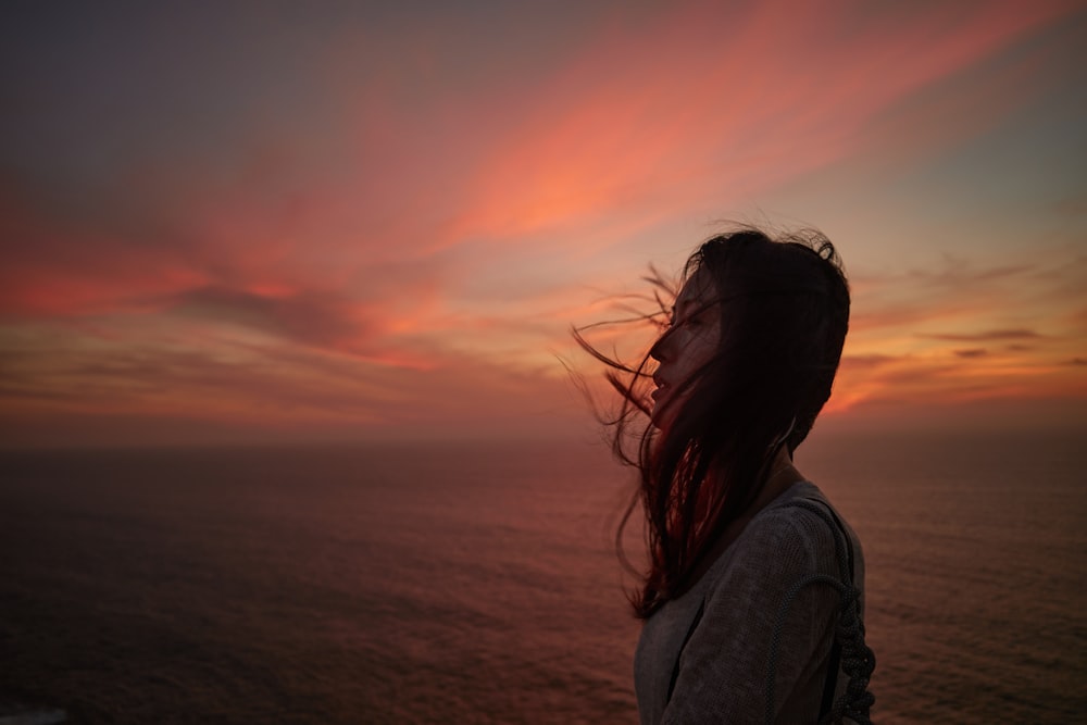 a woman looking out at the ocean at sunset