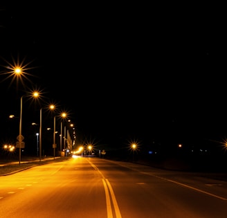 A row of reflective cat eyes embedded along a highway, shining under streetlights at dusk.