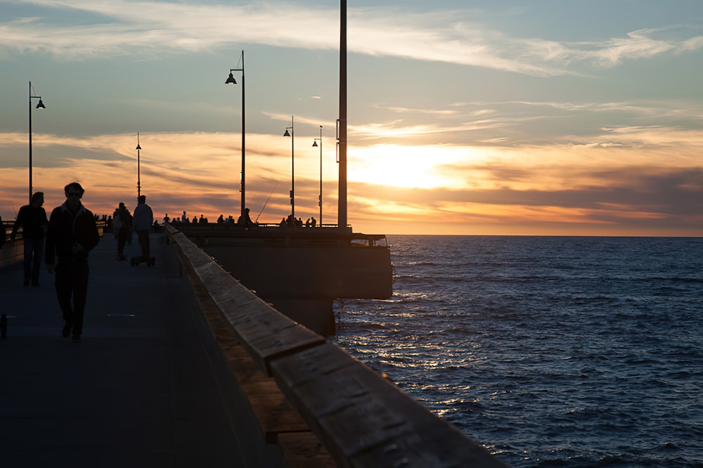 a group of people walking along a pier next to the ocean